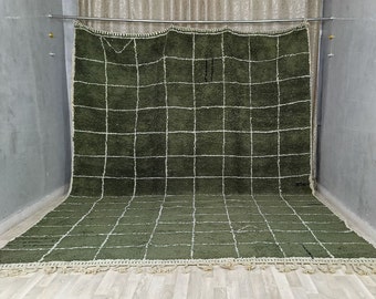 May include: A large, olive green rug with a grid pattern of white lines. The rug has a thick, textured pile and a fringe along the bottom edge. The rug is displayed against a neutral background.