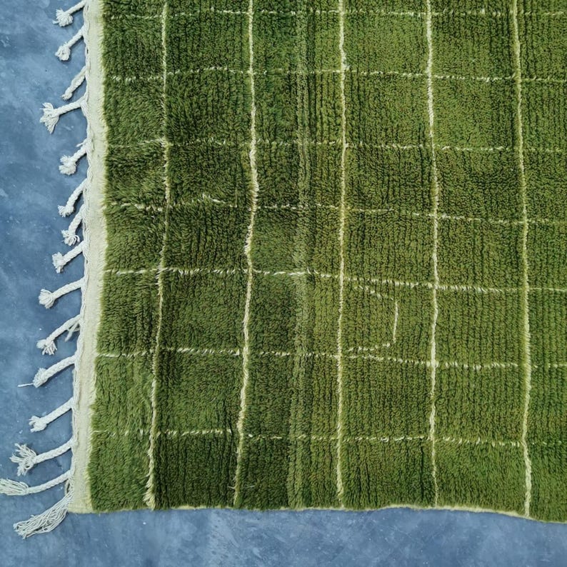 May include: A close-up of a green rug with a grid pattern. The rug has a shaggy texture and is a deep shade of green. White lines form the grid, and the edge has a white fringe.