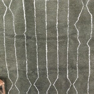 May include: Olive green rug with a geometric pattern. The rug has vertical white lines and diamond shapes. It has a soft, textured appearance, suggesting comfort. A decorative floor covering, suitable for a living space.