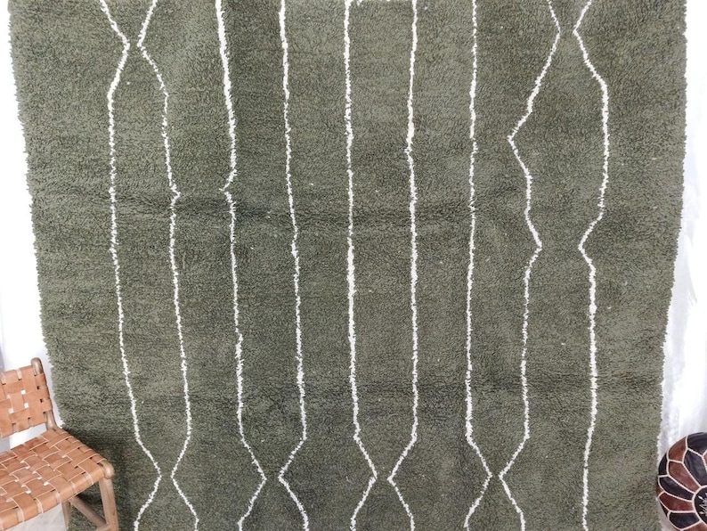 May include: Olive green rug with a geometric pattern. The rug has vertical white lines and diamond shapes. It has a soft, textured appearance, suggesting comfort. A decorative floor covering, suitable for a living space.