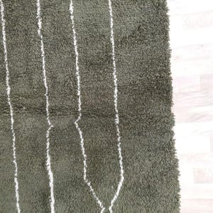 May include: Close-up of a green rug featuring white vertical stripes and diamond patterns. The rug has a shaggy texture, suggesting a soft material. The design is simple and modern, suitable for various interior styles.