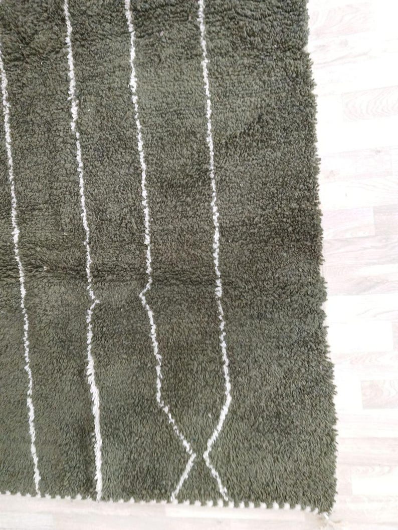 May include: Close-up of a green rug featuring white vertical stripes and diamond patterns. The rug has a shaggy texture, suggesting a soft material. The design is simple and modern, suitable for various interior styles.