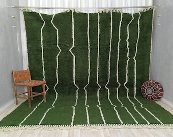 May include: A large, green rug with vertical white lines and a fringed edge. A woven wooden chair and a round leather ottoman are in the background. The rug is a prominent feature, adding a touch of color and texture to the space.