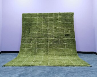 May include: A large, rectangular green rug with a grid pattern. The rug is a solid shade of green with a textured surface. The grid lines are a lighter shade of green. The rug is displayed against a purple wall and a blue floor.