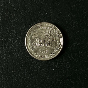 May include: A silver-colored United States quarter dollar coin featuring a portrait of Edith Kanakaʻole with a lei on her head. The text reads UNITED STATES OF AMERICA, EDITH KANAKAʻOLE, 25¢, E PLURIBUS UNUM, and the Hawaiian phrase E hō mai ka ʻike.