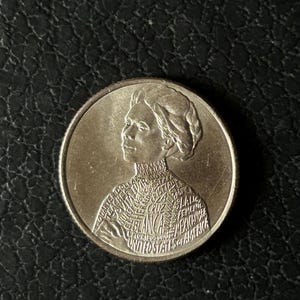 May include: A silver-colored United States quarter dollar coin featuring a profile portrait of Jovita Idar. The surface of the coin is engraved with text including her name, her roles as a teacher and nurse, and the phrase United States of America.