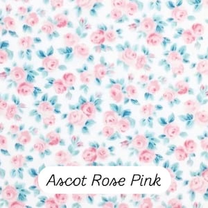 May include: A fabric with a repeating floral pattern of pink roses and blue-green leaves on a white background. The text "Ascot Rose Pink" is displayed in a white rectangle at the bottom of the image.