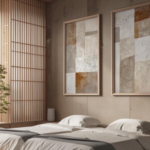 May include: Two abstract paintings with a beige and brown color scheme hang on a wall above a bed with white linens. The bed is in a room with a wooden slatted wall.