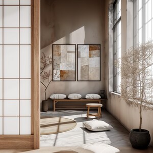 May include: A minimalist living room with a wooden bench and a round stool. Two abstract paintings hang on the wall, and a small tree is in the corner. The room has a light and airy feel.