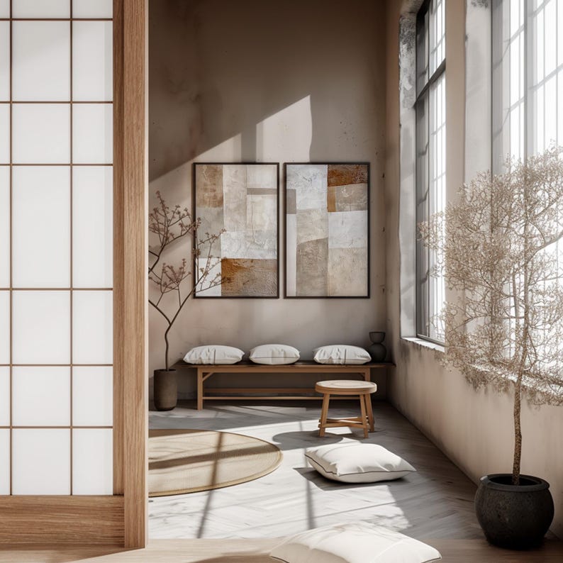 May include: A minimalist living room with a wooden bench and a round stool. Two abstract paintings hang on the wall, and a small tree is in the corner. The room has a light and airy feel.