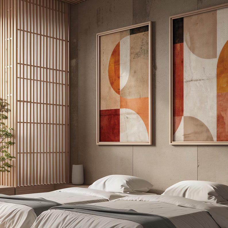 May include: Two framed abstract art prints with geometric shapes in shades of orange, red, and beige. The artwork is displayed on a neutral-colored wall above a bed with white bedding. The room features a wooden screen and a minimalist aesthetic.
