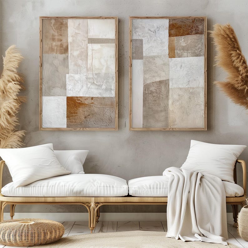 May include: Two framed abstract paintings with a geometric design in shades of brown, beige, and white. The paintings are hanging on a light gray wall above a white couch with a white throw blanket.