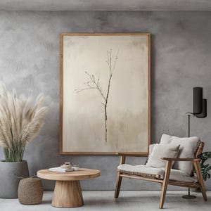 Pode incluir: Uma sala de estar minimalista com uma mesa de centro de madeira marrom claro, uma cadeira de vime com uma almofada branca e uma impressão emoldurada de um ramo delicado sobre um fundo bege.