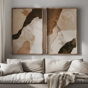 May include: Two abstract art prints in wooden frames. The prints feature a brown, beige, and white color scheme with abstract shapes and textures.