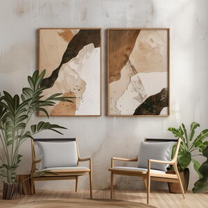 May include: Two abstract paintings with brown, beige, and black colors in wooden frames hanging on a white wall above two wooden chairs with gray cushions.