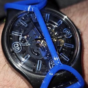 May include: A black wristwatch with a skeleton dial featuring blue hour markers and hands. A bright blue, Y-shaped plastic frame is attached over the watch face, extending from the top to the bottom of the watch case, securing over the black strap.