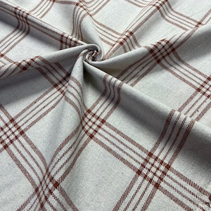 May include: Close-up of a fabric with a plaid pattern. The fabric is a light beige color with a repeating pattern of dark brown lines. The lines intersect to create a grid-like design. The fabric is folded and twisted in the center.