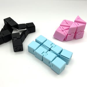 May include: Three fidget toys in black, light blue, and pink. The black toy is in a star shape. The light blue toy is a straight line of cubes. The pink toy is a triangular shape. All toys are made of plastic.