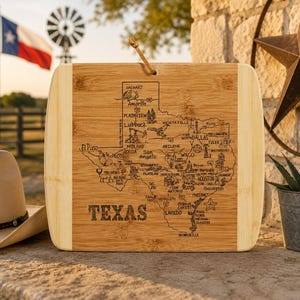 May include: A rectangular wooden chopping board with rounded corners, featuring a detailed map of Texas. The map includes city names and is etched into the light brown wood. The word "TEXAS" is displayed prominently.