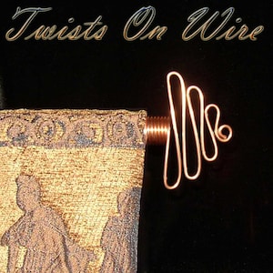 May include: A copper wire tapestry rod with a decorative, twisted design. The rod is attached to a tapestry with a gold and brown pattern.