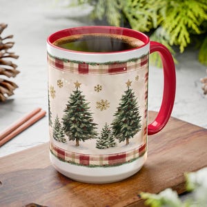 May include: A large white ceramic mug with a red interior and handle, filled with coffee. The mug features a Christmas tree design with snowflakes and stars, framed by a red and beige plaid pattern. The mug is on a wooden cutting board.