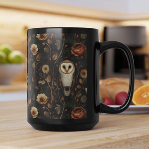 May include: Black ceramic coffee mug featuring a floral pattern with roses, sunflowers, and an owl illustration. The mug has a large handle and a dark background. A kitchen countertop is in the background.
