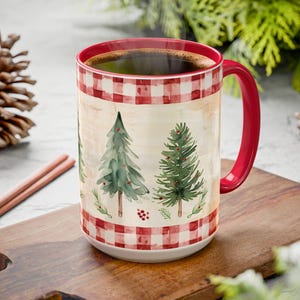 May include: A ceramic mug featuring a red and white checkered pattern at the top and bottom rims. The center displays watercolor-style illustrations of green pine trees with small red accents. The mug has a solid red handle and a red interior.