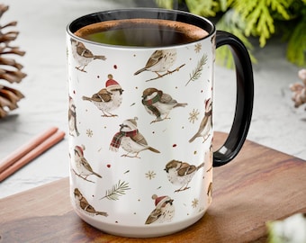 May include: A white ceramic mug with a black interior and handle, featuring a repeating pattern of small brown sparrows. Some birds wear red winter hats or scarves. The design includes small green pine sprigs and gold snowflakes.