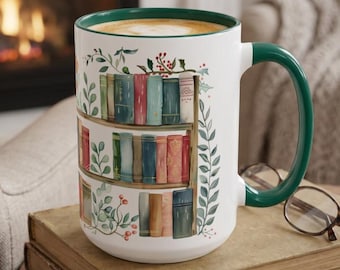 May include: A white ceramic mug with a dark green handle and interior rim, featuring a wrap-around illustration of three wooden shelves filled with colorful books, accented by green leafy vines and small red berries on the exterior.