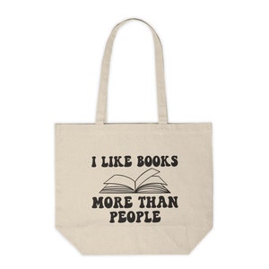 May include: A beige tote bag with black text that reads "I like books more than people" and a black illustration of an open book.