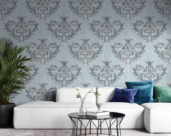 May include: A white sectional sofa with blue and green throw pillows sits in front of a wall with a blue and gray damask wallpaper pattern. A black metal coffee table with a glass top sits in front of the sofa. A vase with white flowers sits on the coffee table.