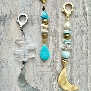 May include: Three keychains with decorative beads and charms. One has a silver crescent moon charm and clear crystal beads. Another features turquoise and gold beads with a turquoise teardrop charm. The third has a gold crescent moon charm and a mix of beads.