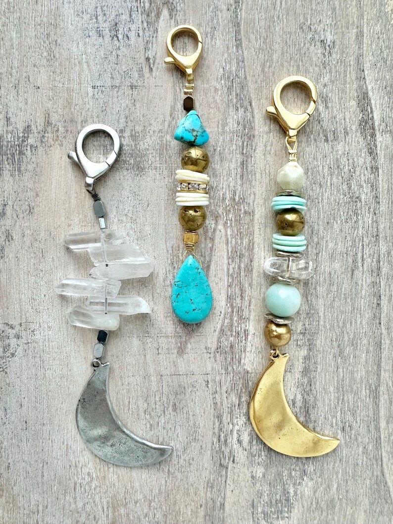 May include: Three keychains with decorative beads and charms. One has a silver crescent moon charm and clear crystal beads. Another features turquoise and gold beads with a turquoise teardrop charm. The third has a gold crescent moon charm and a mix of beads.