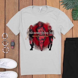 May include: A gray t-shirt with a graphic of three figures in red and black superhero costumes. The text on the shirt reads "They say I did something bad. Then why still feel so good?"