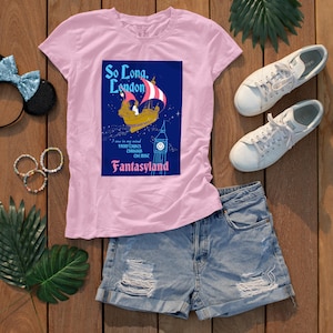 May include: A light pink t-shirt featuring a graphic with the text "So Long, London" and a ship sailing in the sky. The graphic also includes the text "Fantasyland" and a clock tower. The shirt is paired with denim shorts and white sneakers.