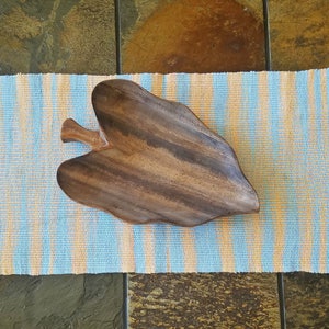 May include: A wooden leaf-shaped serving bowl on a blue and orange striped placemat.