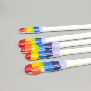 May include: Five white glass stirring sticks with rainbow colored stripes. The stripes are red, orange, yellow, green, blue, and purple.