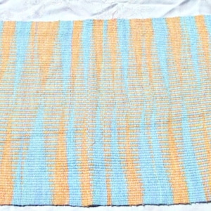 May include: A woven rug with a striped pattern in shades of blue and orange. The rug has a fringed edge.