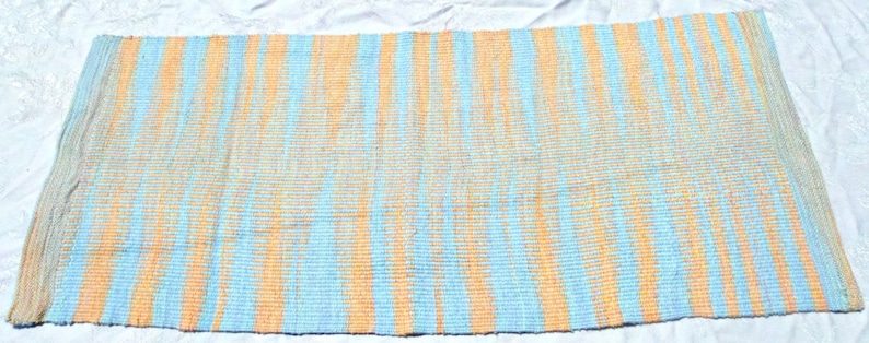 May include: A woven rug with a striped pattern in shades of blue and orange. The rug has a fringed edge.