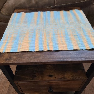 May include: A blue and orange striped woven table runner on a dark brown wooden table with a drawer. The table has black metal legs.