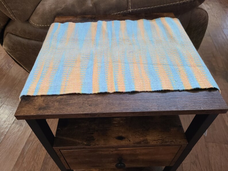 May include: A blue and orange striped woven table runner on a dark brown wooden table with a drawer. The table has black metal legs.
