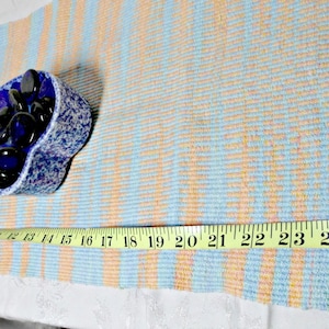 May include: A blue and white woven rug with a measuring tape placed on top. The tape measures 26 inches. A small blue bowl filled with dark blue stones sits on the rug.