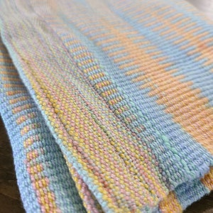 May include: A woven throw blanket with a blue, yellow, and pink striped pattern. The blanket is folded in half and the edges are visible.