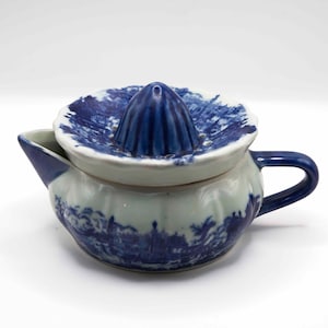 May include: A ceramic citrus juicer with a blue and white design. The juicer features a reamer, a bowl, a spout, and a handle. The blue and white pattern depicts a landscape scene. The juicer is designed for squeezing citrus fruits.