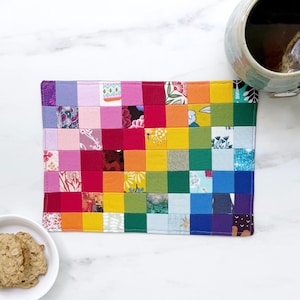 May include: A rectangular fabric mat constructed from a grid of small, multi-coloured squares featuring various floral, geometric, and solid patterns in shades of red, orange, yellow, green, blue, purple, pink, and white with visible stitching.