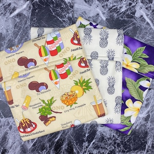 May include: Four fabric pouches with different Hawaiian-themed designs. The pouches are beige with a variety of colorful illustrations of food and drinks, including shaved ice, macadamia chocolate, poi malasada, and ling hing pineapple. The other pouches are purple with white plumeria flowers and green leaves, and beige with pineapple designs.