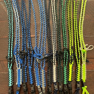 Puede incluir: Una colecci&oacute;n de 12 cordones trenzados en varias combinaciones de colores, incluyendo negro, azul, verde y blanco. Cada cord&oacute;n tiene un clip de pl&aacute;stico negro en el extremo.