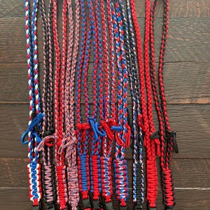 Puede incluir: Una colecci&oacute;n de 13 cordones trenzados en combinaciones de colores rojo, blanco y azul. Los cordones est&aacute;n hechos de paracord y tienen un cierre de pl&aacute;stico negro en el extremo.