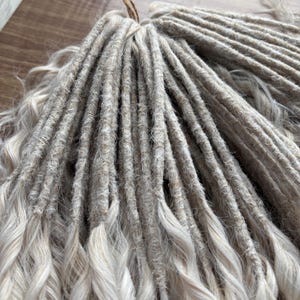 Puede incluir: Un paquete de rastas sint&eacute;ticas de color gris claro y blanco. Las rastas est&aacute;n hechas de un material suave y texturizado y est&aacute;n listas para ser instaladas.