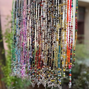 Op de afbeelding: Een display van kleurrijke kralenkettingen die aan een metalen staaf hangen. De kettingen hebben een verscheidenheid aan kralen in verschillende kleuren, waaronder rood, blauw, groen en geel. Sommige hebben zilverkleurige kruisbedels.